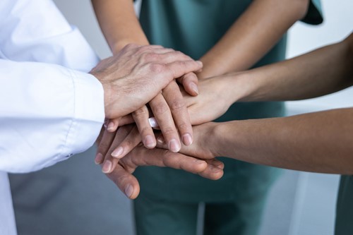 Close-up of healthcare professionals stacking their hands together in a gesture of teamwork.