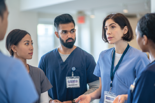 A group of five healthcare providers, one male and three female, listening to one of the female healthcare providers speak.