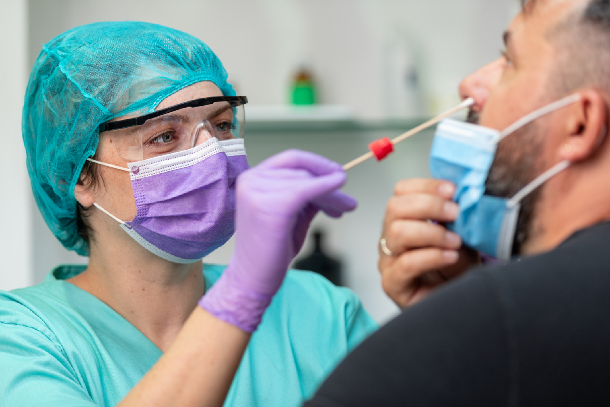 A healthcare worker in protective gear takes nose swab test from a person.